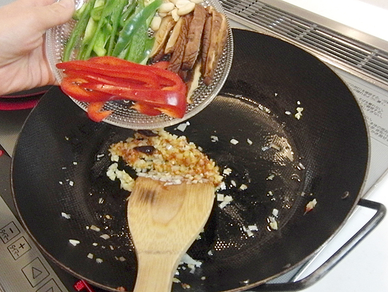 焼き材料を炒めているフライパンに野菜を入れる様子